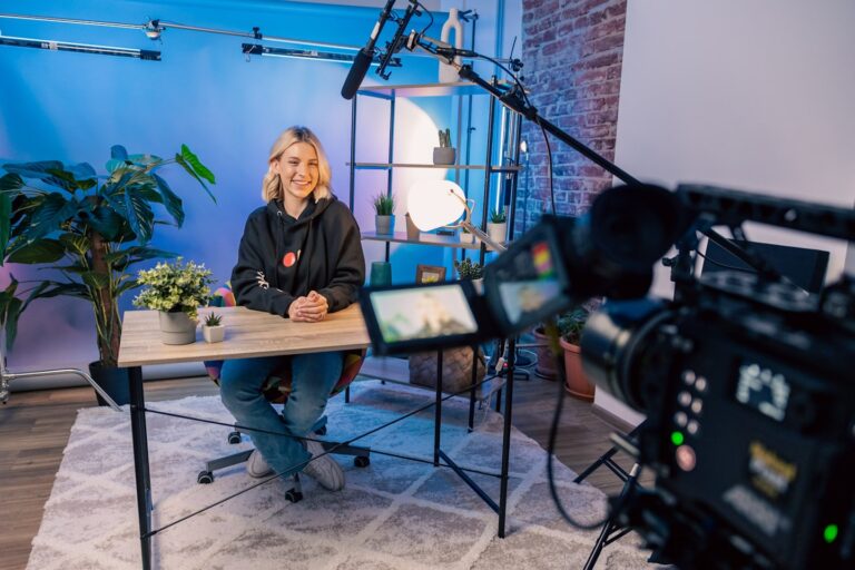Creator in a modern studio beside a screen showing subscription platform management for a paid content site